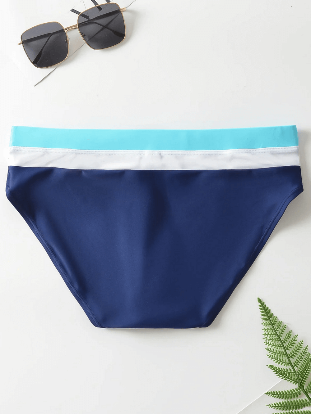 Navy blue men's swim briefs with drawstring waistband, featuring a stylish mid-rise design, laid beside sunglasses on white background.