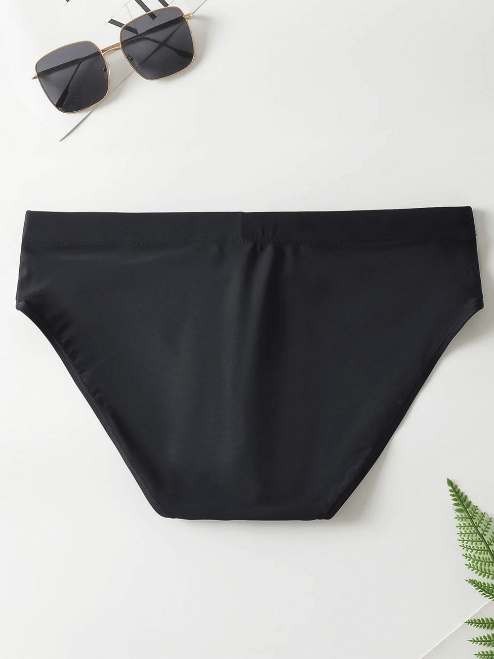 Black men's swim briefs with drawstring waistband, mid-rise style, perfect for beach or pool, paired with sunglasses on a white background.