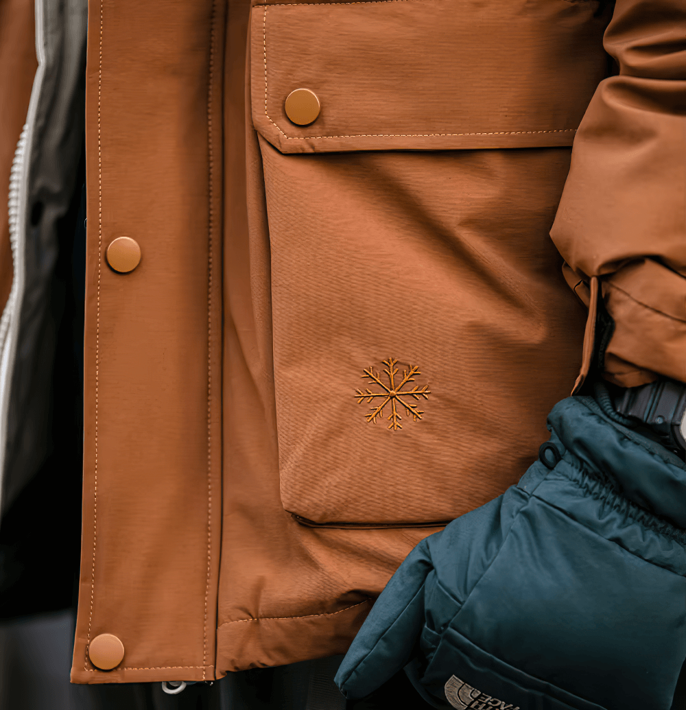 Close-up of men's duck down winter jacket with snowflake detail and gloves, highlighting pocket design and brown fabric texture.