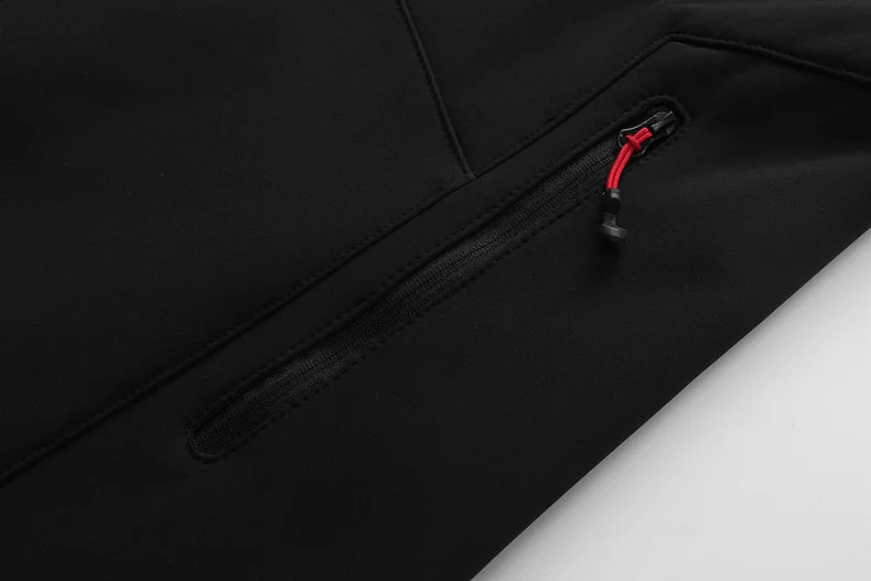 Close-up of Men's Waterproof Softshell Jacket zippered pocket on black fabric, showcasing durable design and red accent for accessibility.