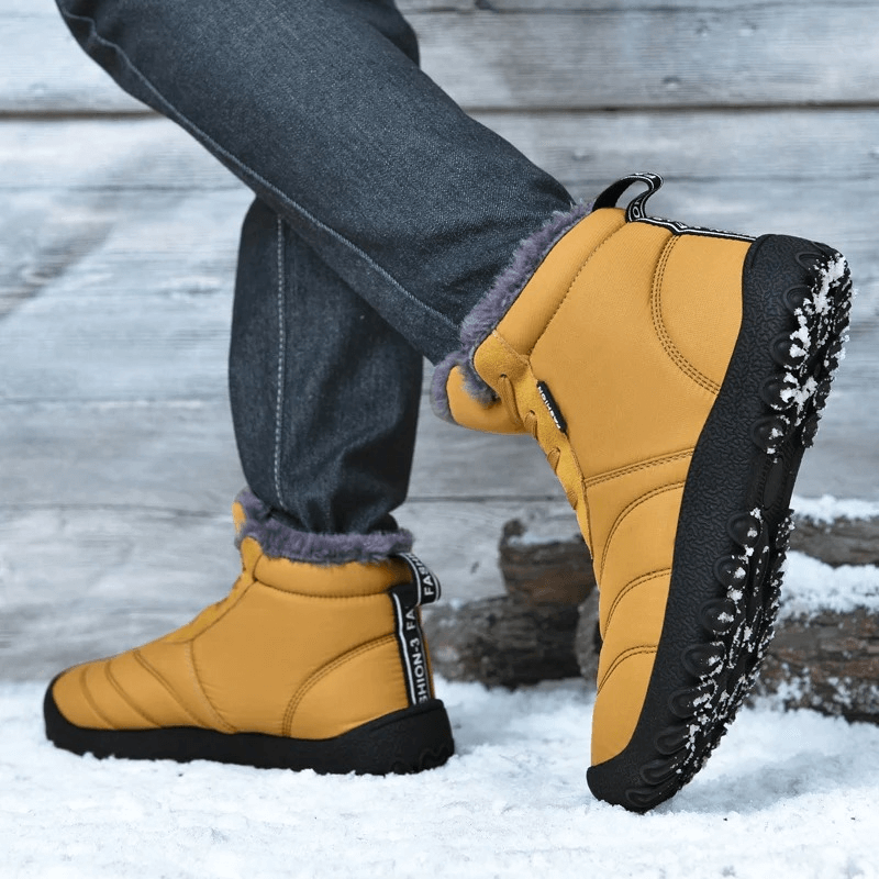 Man wearing mustard yellow winter ankle snow boots with rubber outsole standing on snow, showcasing split leather and lace-up design.