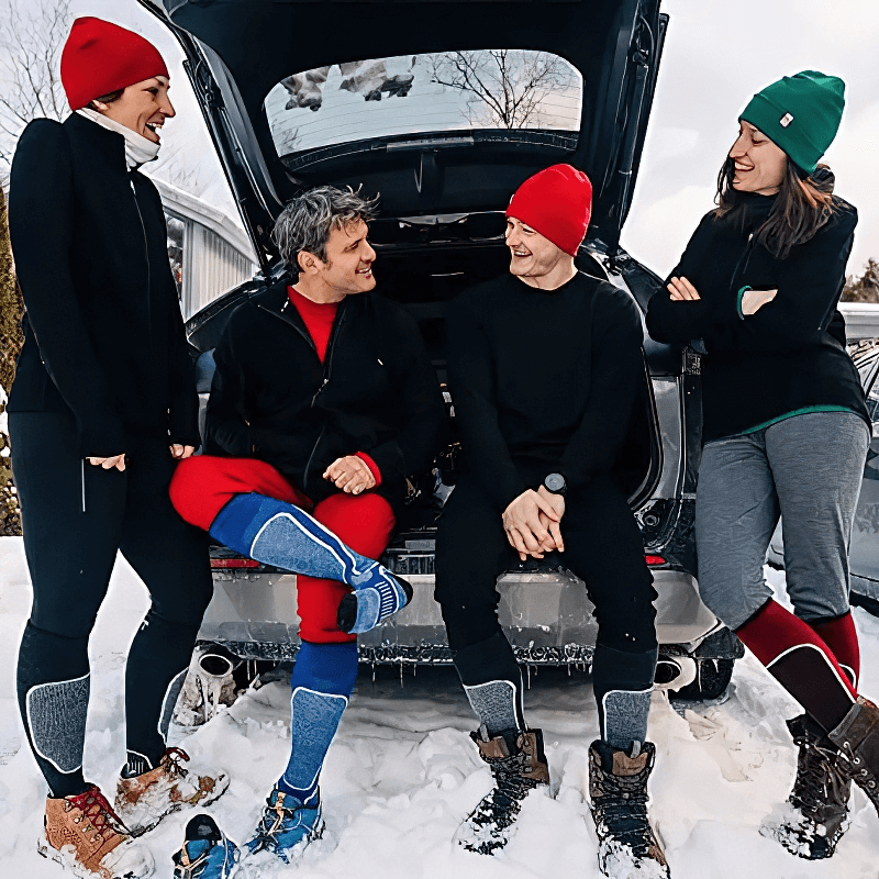 A group of people in winter clothing and merino wool thermal pants having fun by an open car trunk in a snowy setting.