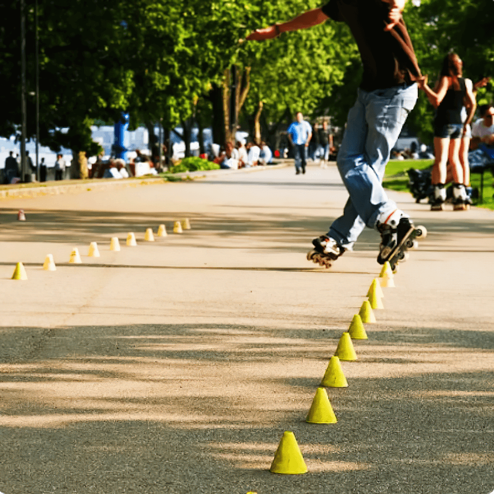 Skater navigating through yellow training cones on a sunny day in a park, demonstrating agility and precision during drills.