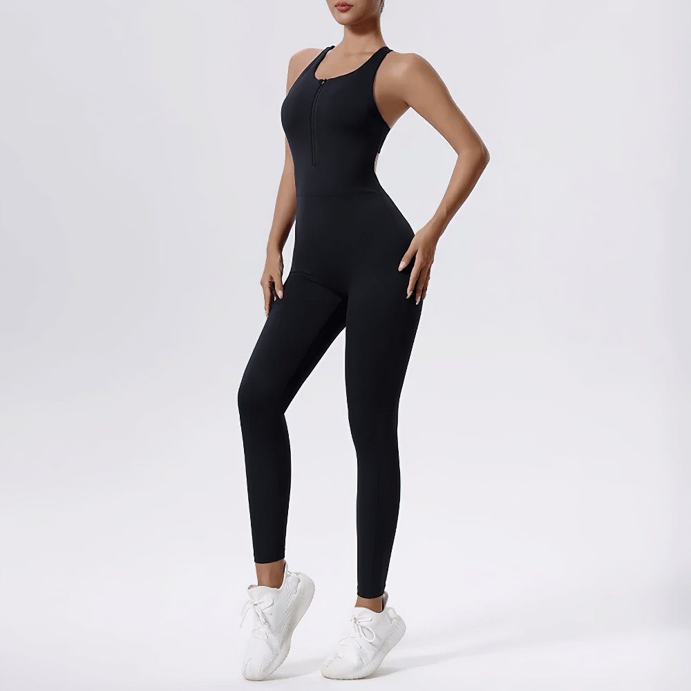 Woman wearing a black zip-front fitness jumpsuit, perfect for gym to street style, showcasing a seamless, sleeveless design with white trainers.