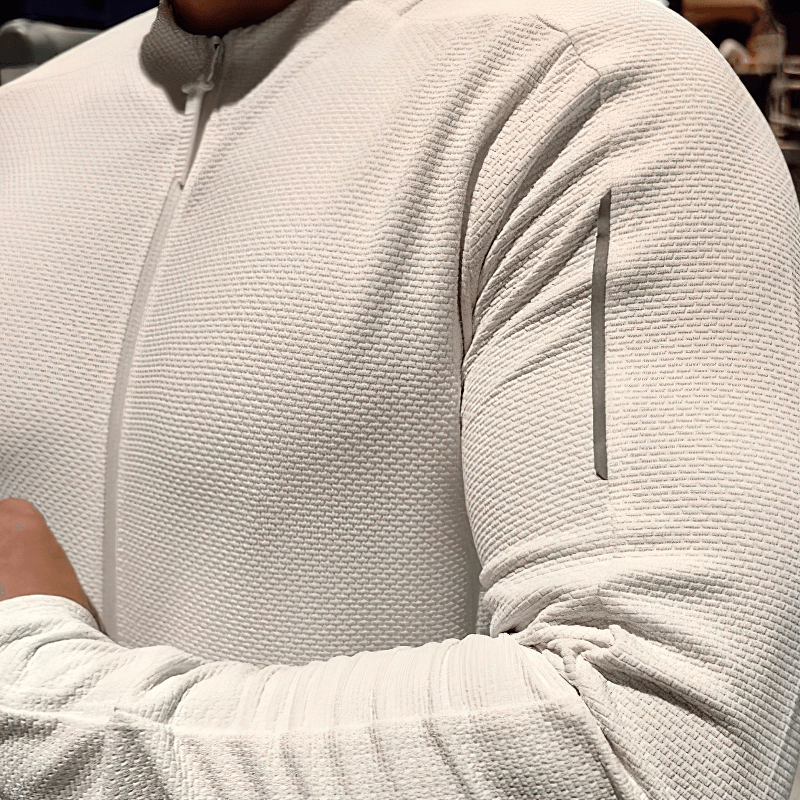Close-up of textured zip-up sports jacket in light color with arm pocket, showing modern design and breathable fabric.