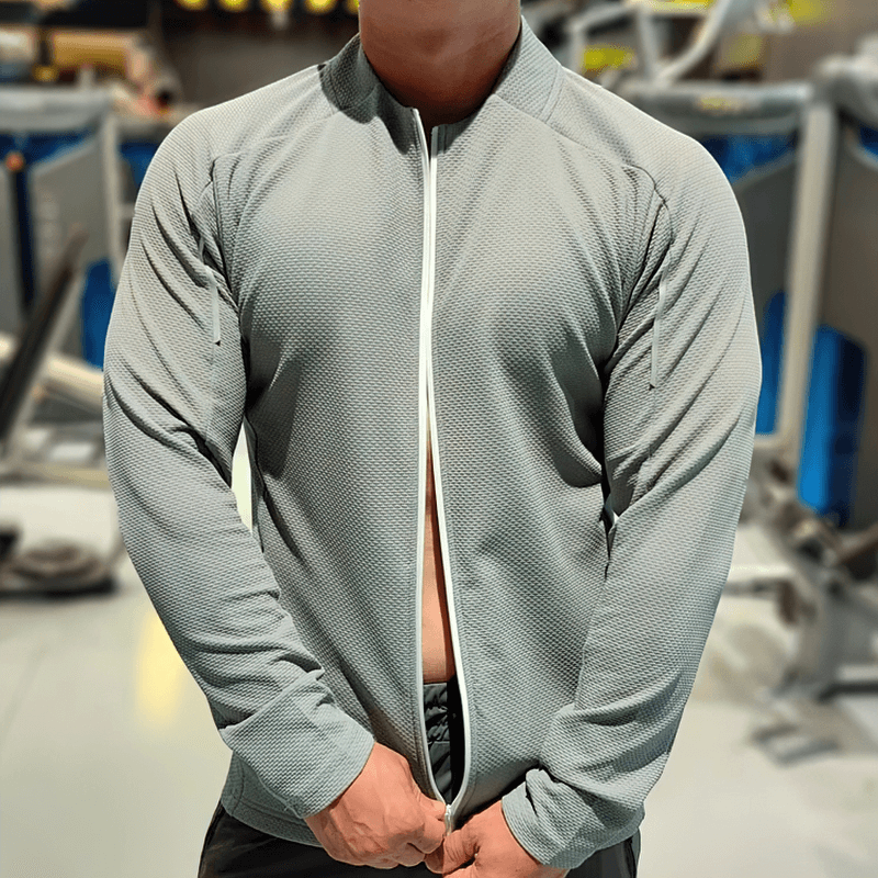 Man wearing modern zip-up textured sports jacket in gym, showcasing breathable fabric and sleek design, perfect for activewear.