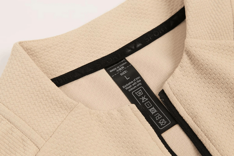 Close-up of textured sports jacket's O-neck collar and clothing label, showcasing breathable cotton-spandex fabric in beige.