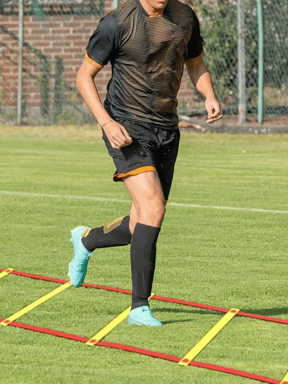 Athlete training with a modular agility ladder featuring red webbing and frosted rungs on a grassy field.