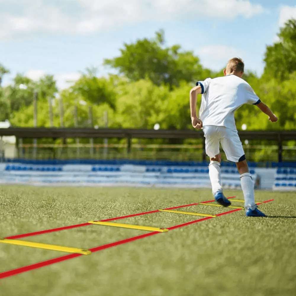 Child practicing soccer footwork on a modular agility ladder with frosted rungs, on a sunny outdoor field.