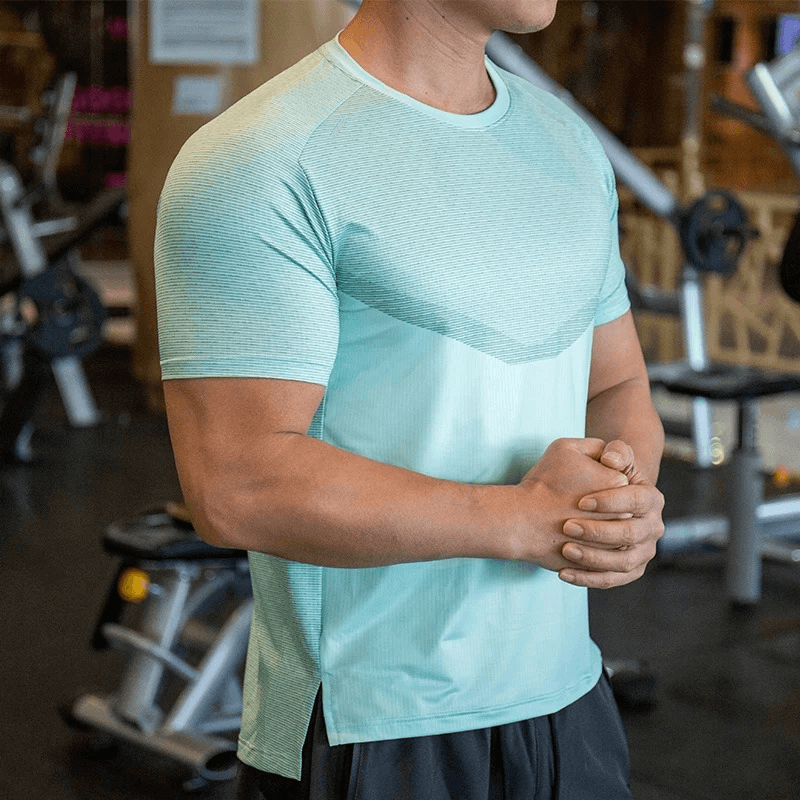Man wearing a moisture-wicking athletic t-shirt in gym, showcasing polyester fabric and O-neck design for active lifestyle performance.