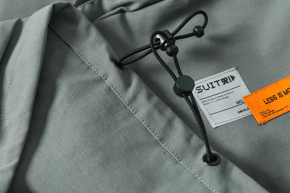 Close-up of a gray multi-pocket utility jacket with drawstring and label, perfect for outdoor adventures and functional fashion.