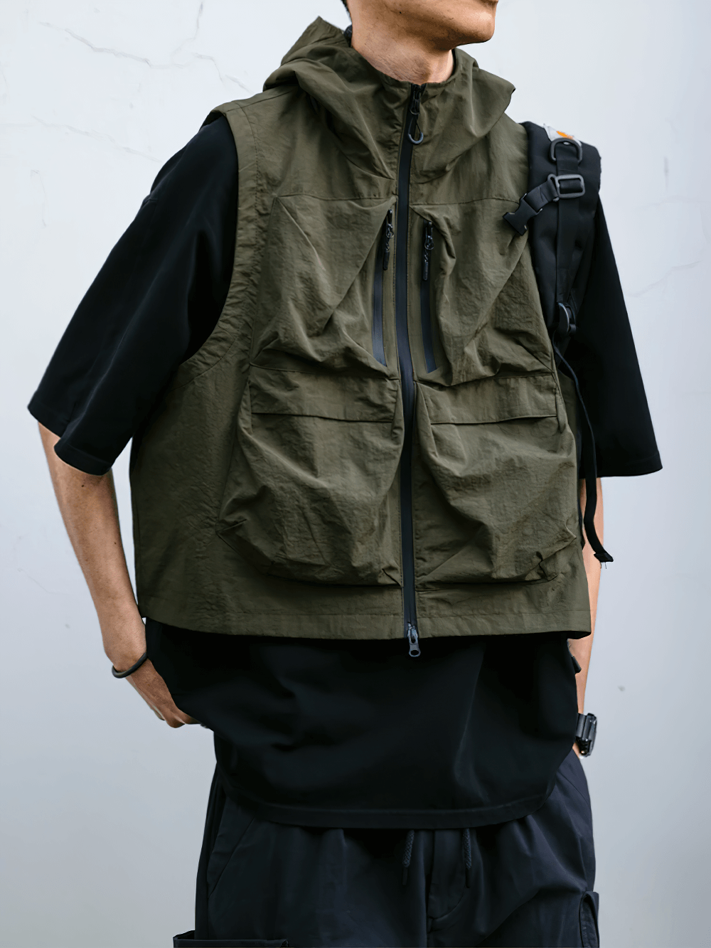 Man wearing a green multi-pocket waterproof cargo vest with hood, suitable for outdoor activities. Stylish and functional design.
