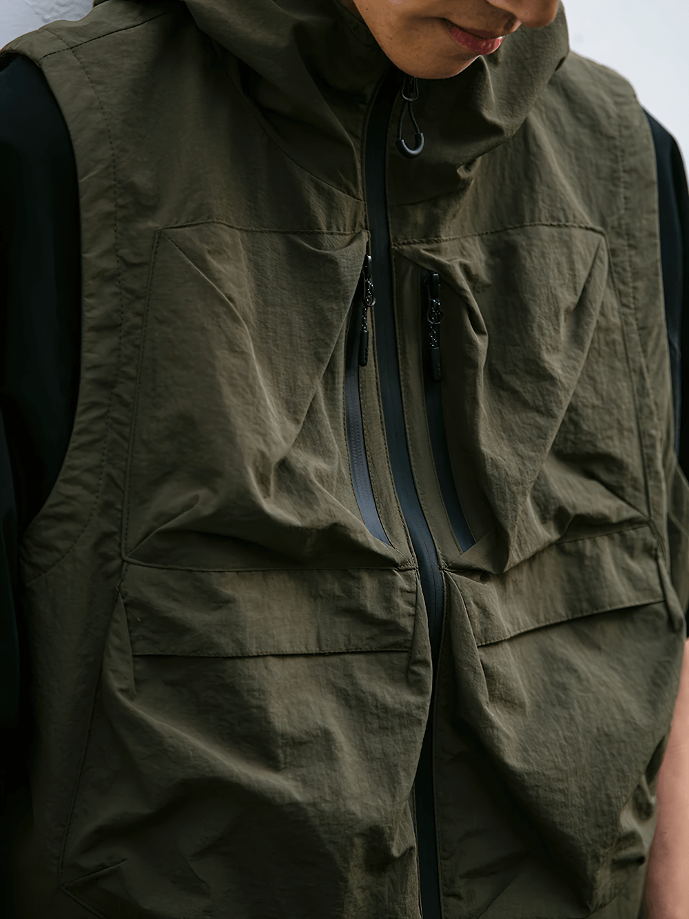 Man wearing a stylish waterproof cargo vest with multiple pockets and hood, ideal for outdoor activities, made of durable nylon fabric.