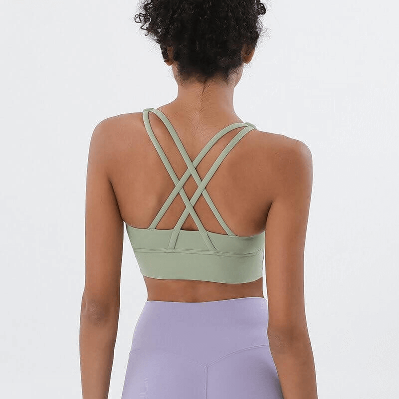 Back view of woman wearing green nylon sports top with cross shoulder straps for yoga and fitness activities.