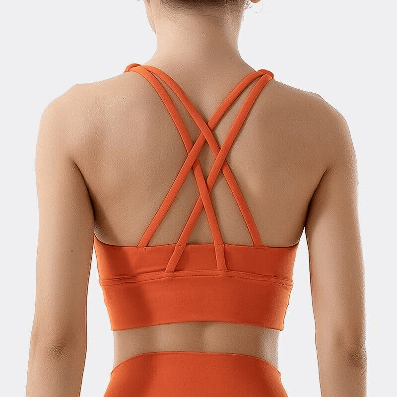 Back view of woman wearing an orange nylon sports top with cross shoulder straps, designed for fitness and comfort.
