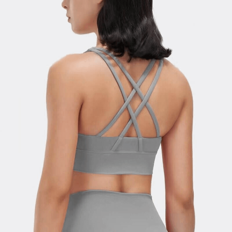 Woman wearing grey nylon sports top with cross-shoulder straps, showing back view. Ideal for yoga, gym, and fitness activities.