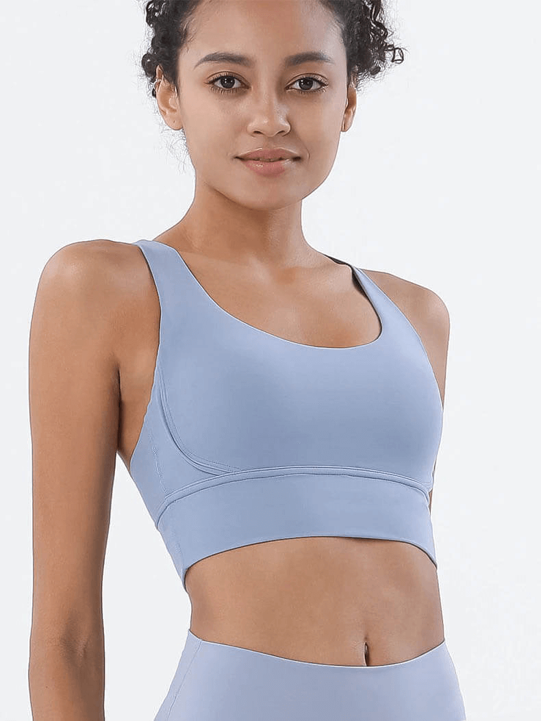Woman wearing a light blue nylon sports top with cross shoulder straps, perfect for yoga and gym sessions.
