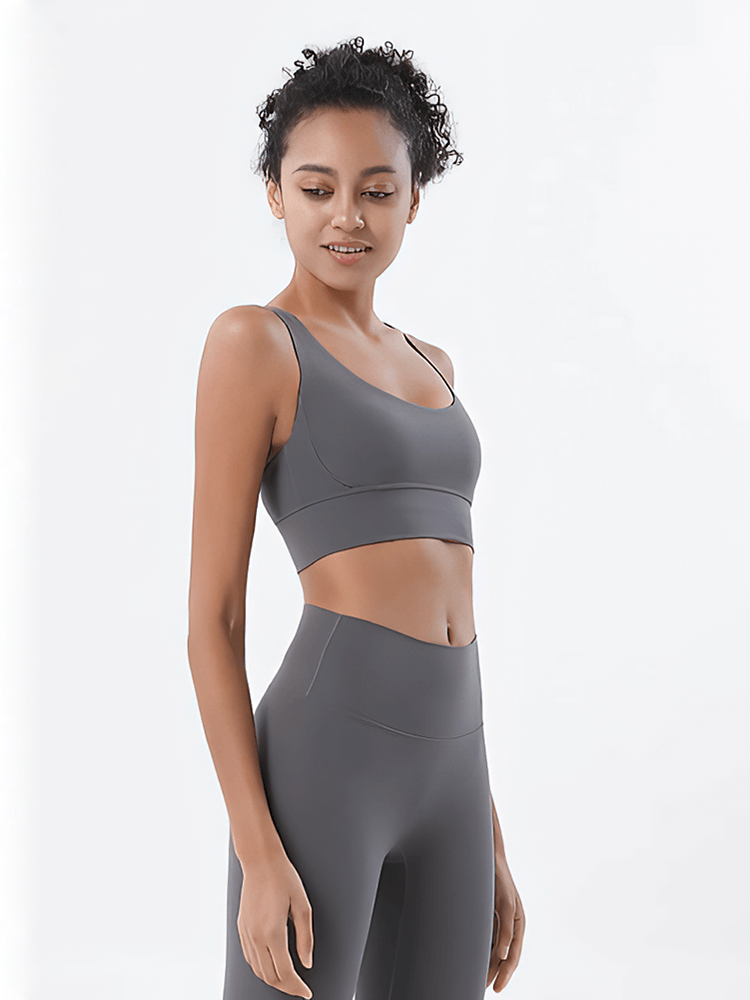 Woman wearing a grey nylon sports top with cross shoulder straps, ideal for yoga and fitness activities.