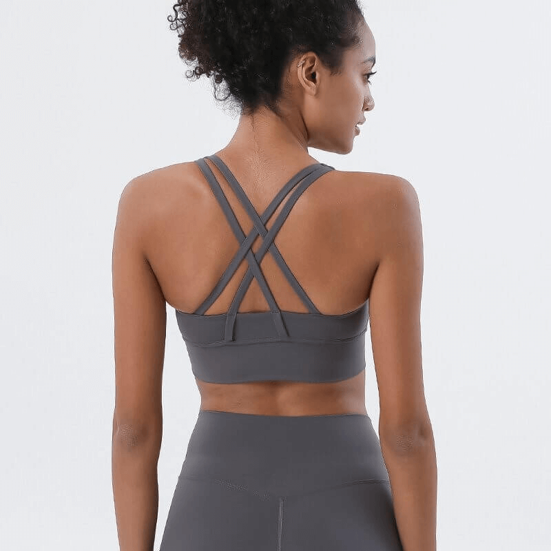 Back view of woman wearing grey nylon sports top with cross-shoulder straps, perfect for yoga and fitness.