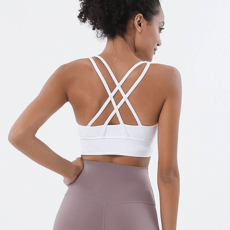 Woman wearing white nylon sports top with cross shoulder straps, perfect for yoga and gym. Stylish and breathable fitness bra.
