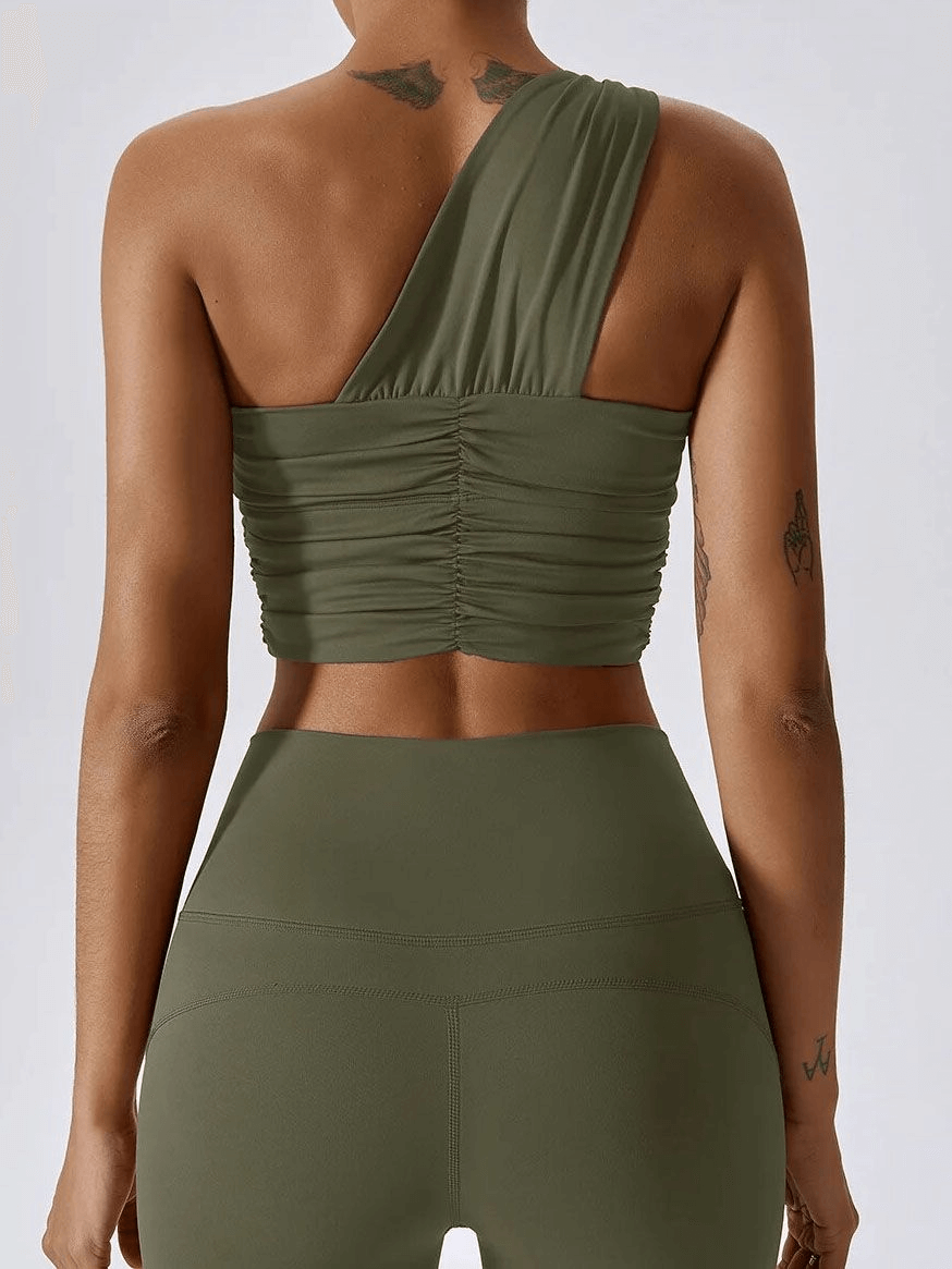 Woman wearing one shoulder backless fitness yoga sports bra in green, showcases comfortable and flexible design for workouts.