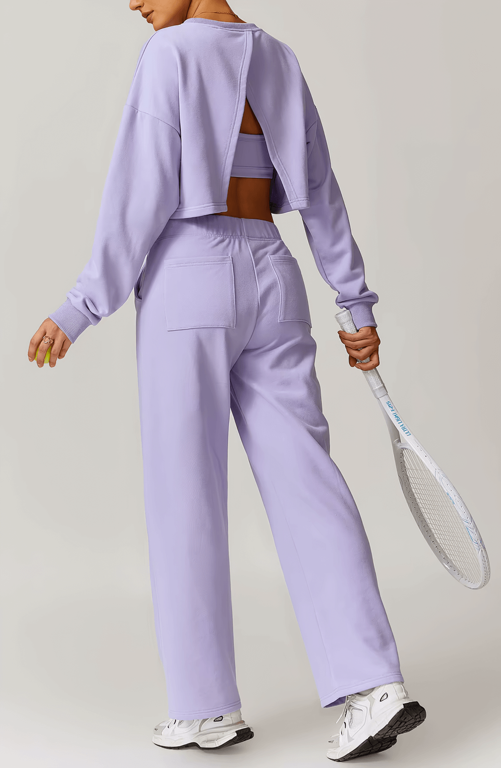 Active woman wearing lavender open-back sweatshirt holding a tennis racket, showcasing stylish and functional sportswear for women.