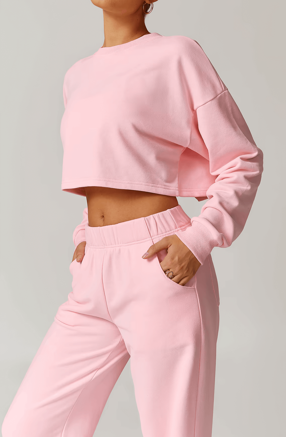 Woman wearing pink crop top and joggers with hands in pockets, showcasing trendy loungewear style.