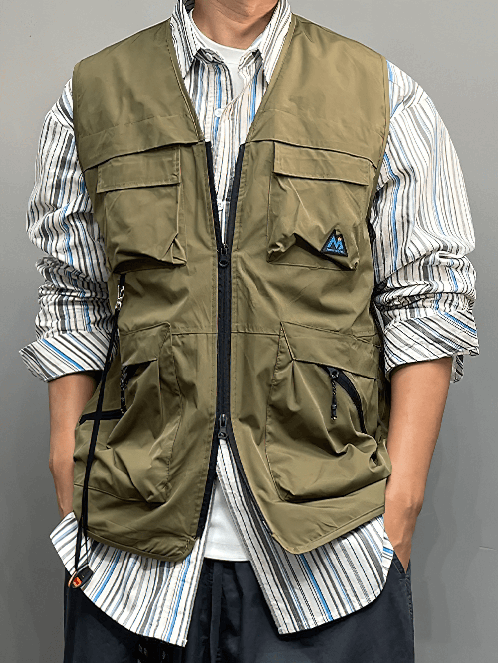 Person wearing a lightweight, multi-pocket outdoor utility vest for hiking or fishing, styled over a striped shirt.