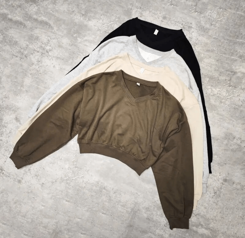 Four cotton sweatshirts in brown, gray, beige, and black, neatly stacked on a gray surface.