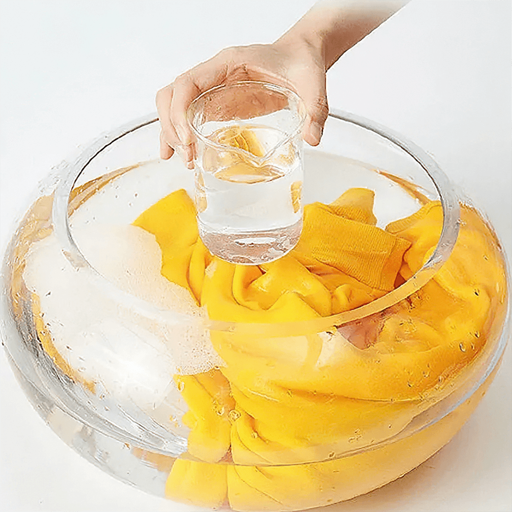 Hand pouring water into a clear bowl with a bright yellow sweater, demonstrating gentle wash care.