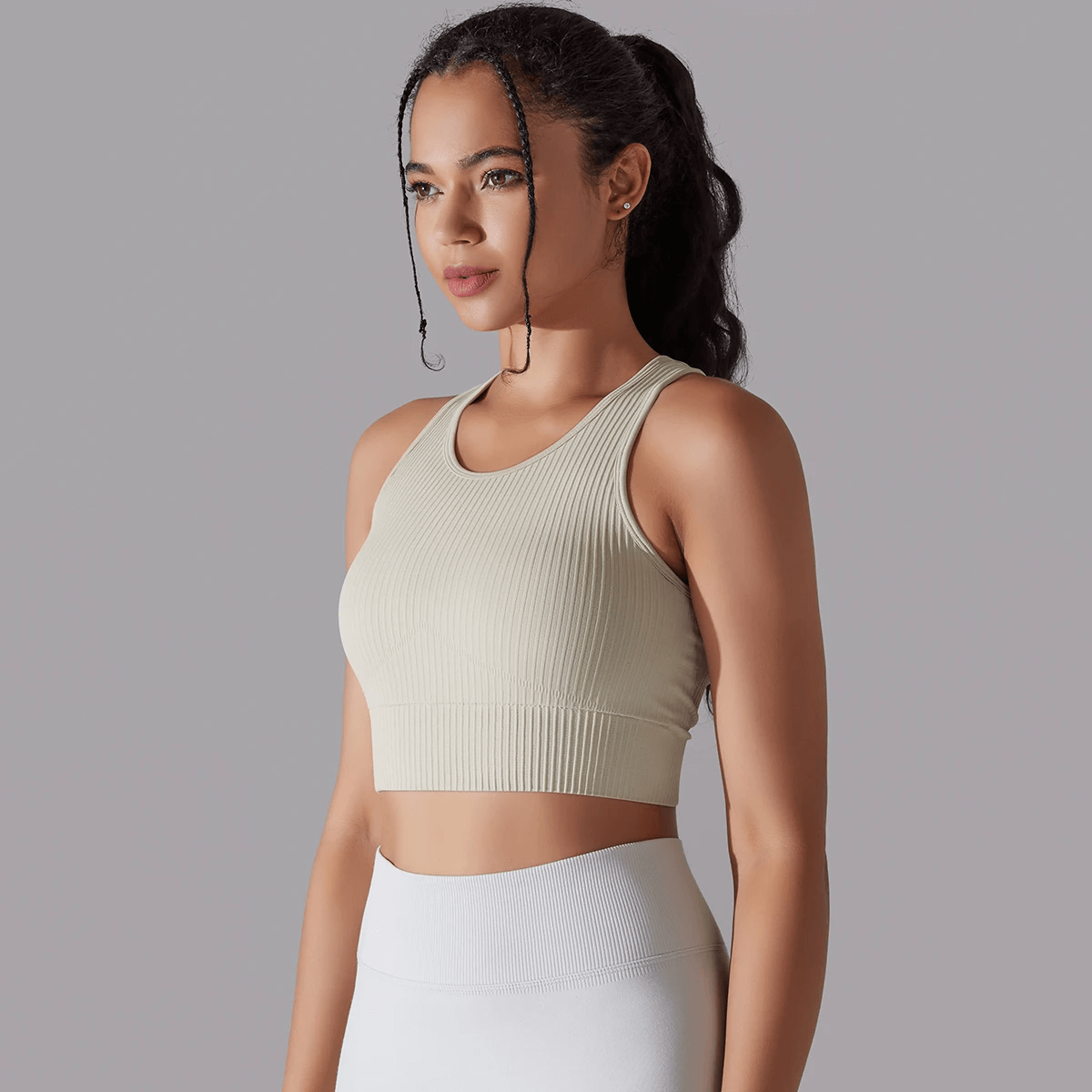 Woman wearing a beige ribbed yoga short tank top, perfect for sports and active wear, showcasing a snug fit with breathable, knitted fabric.