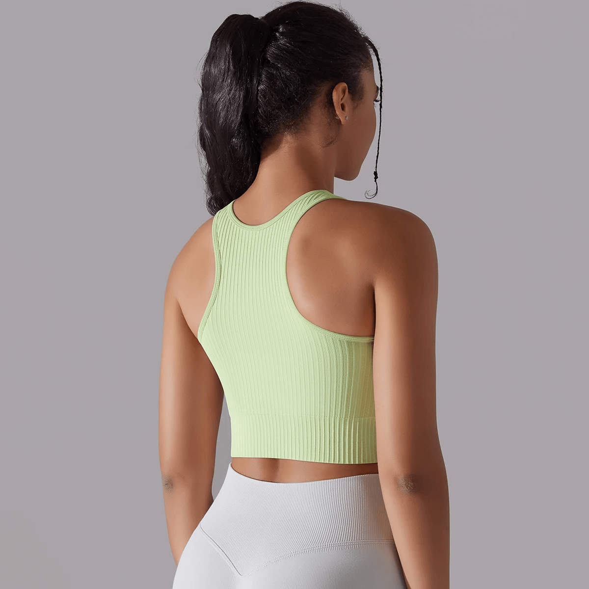 Woman wearing a green ribbed yoga tank top, showing the back view. Ideal for yoga with breathable, knitted fabric.