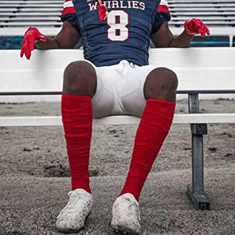 Athlete wearing red knee-high rugby socks with durable ribbed design for performance and style, seated on a bench.