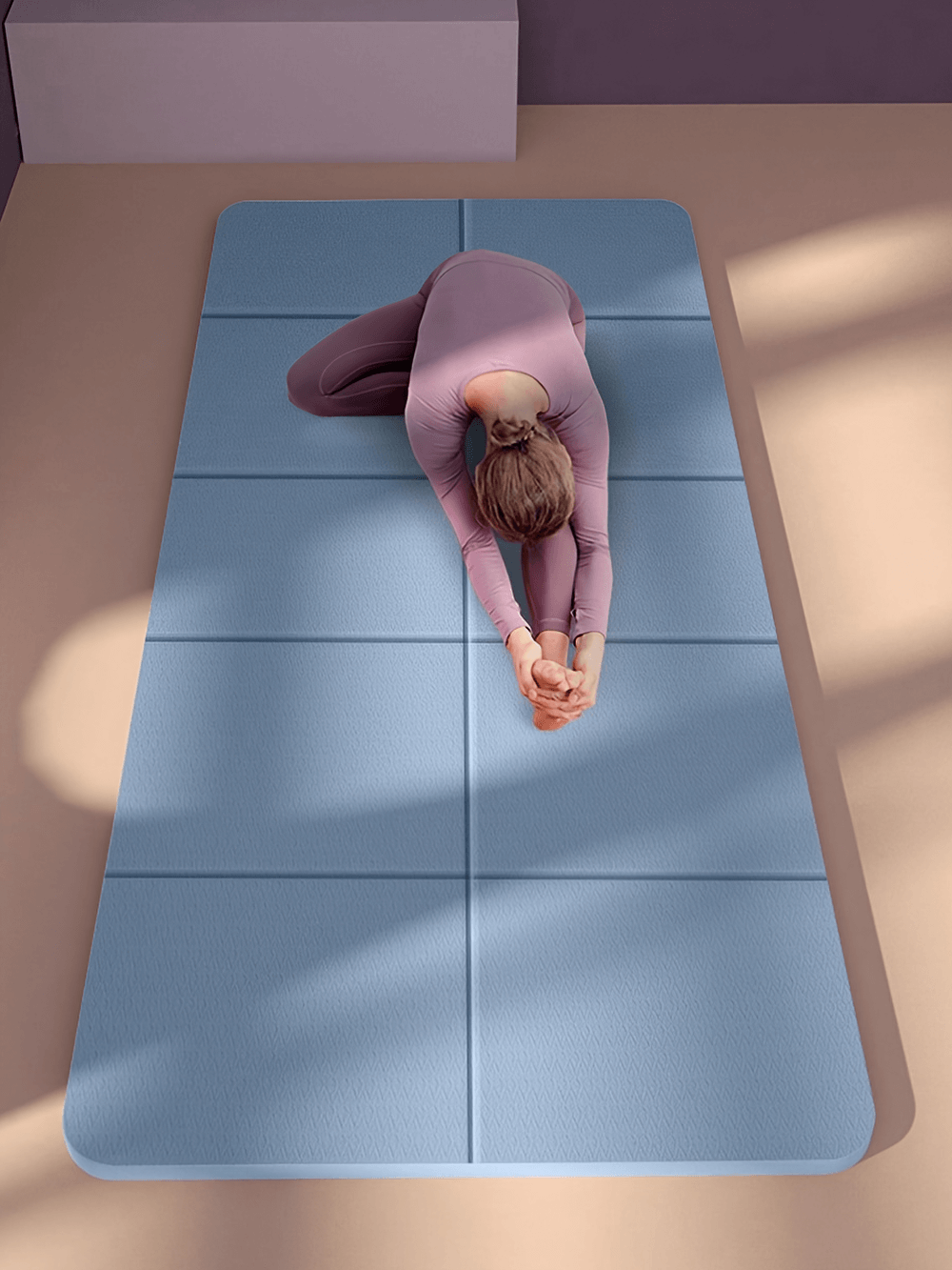 Woman practicing yoga on a blue foldable yoga mat in a sunlit room, highlighting non-slip durable TPE design for stability and comfort.