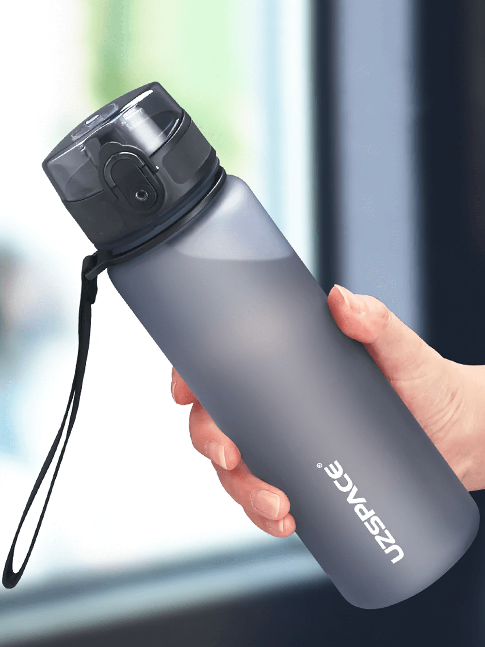 Person holding a portable Tritan sports water bottle with strap and leak-proof lid, ideal for outdoor activities.