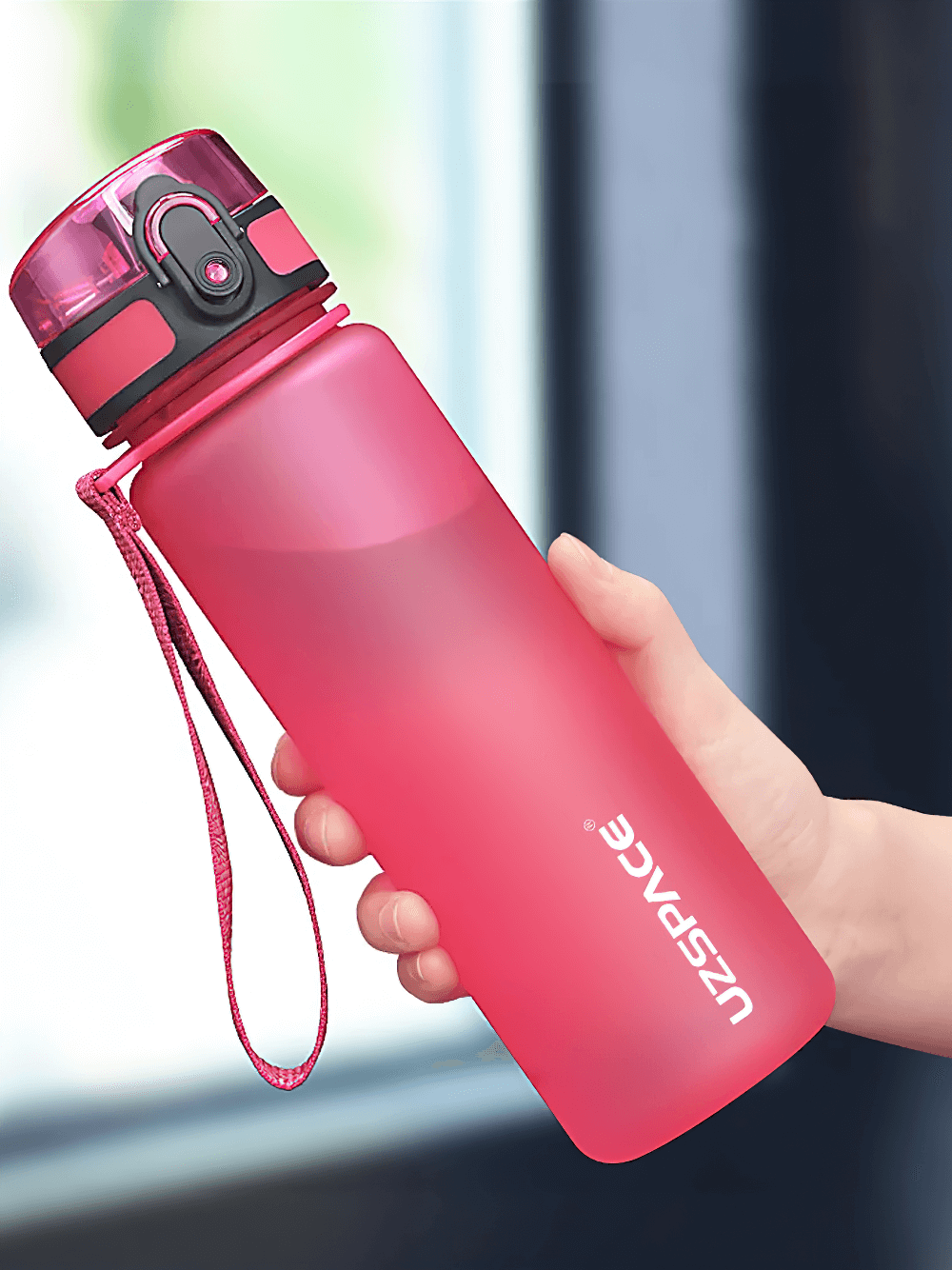 Person holding a pink portable leak-proof sports water bottle with strap, perfect for outdoor activities.