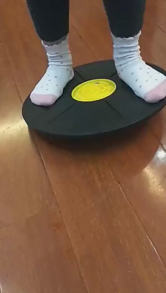 Person balancing on wobble disc trainer with built-in maze game, enhancing core strength and stability on wooden floor.