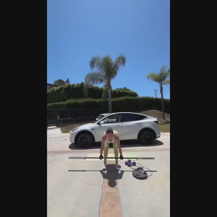 Person lifting a barbell outdoors with a white car and palm trees in the background.