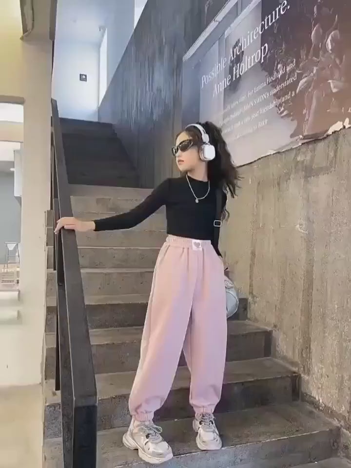 Stylish girl wearing pink loose sports pants with headphones, showcasing a trendy look. Perfect for casual outings and active days.