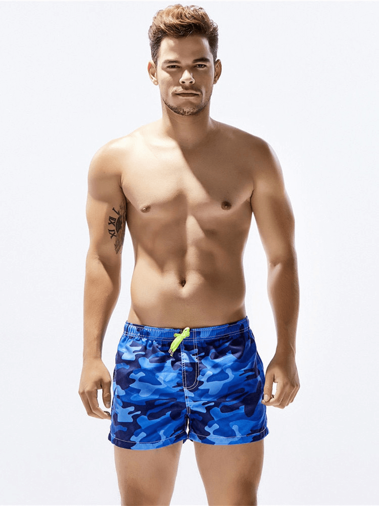 Man wearing blue camouflage print short boardshorts with drawstring waist, perfect for beachwear and quick drying comfort.