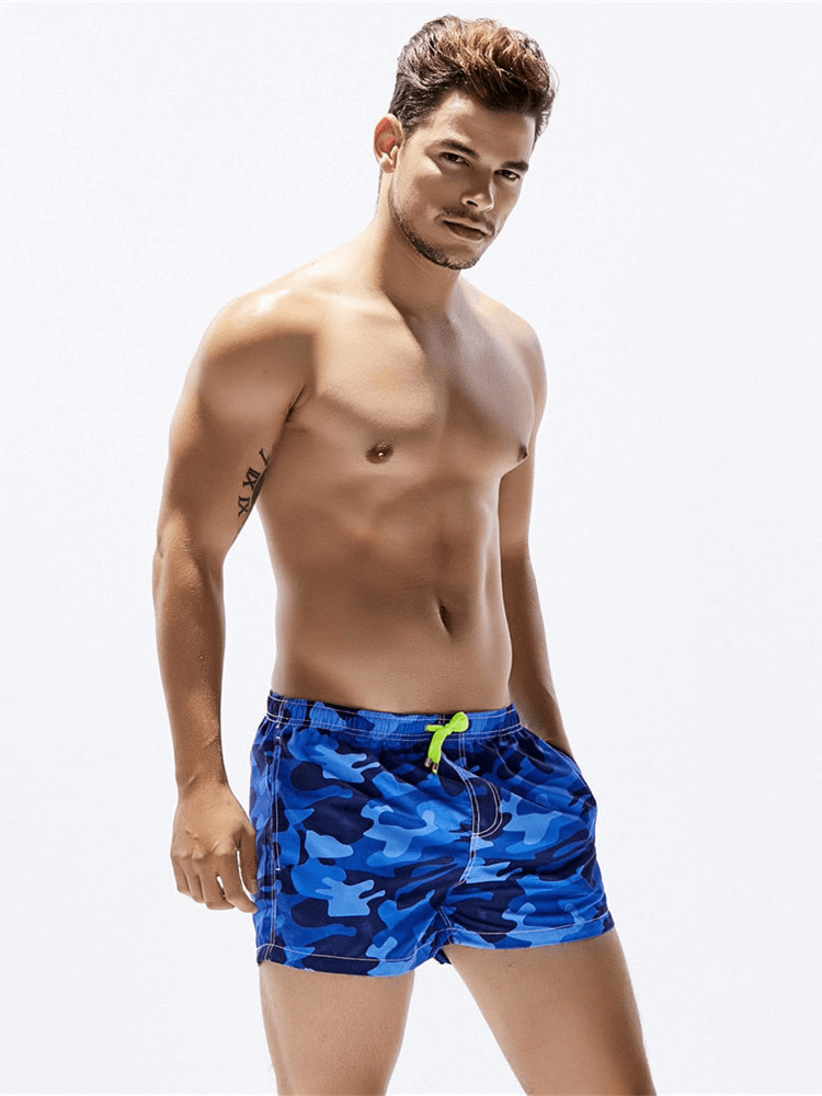 Blue camouflage short boardshorts for men, perfect beachwear with secure drawstring, modeled by a man against a white background.
