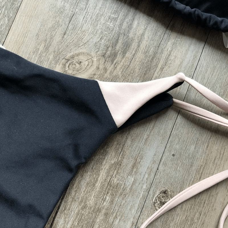 Close-up of sexy lace-up black swimsuit top with soft pink straps on a rustic wooden background.
