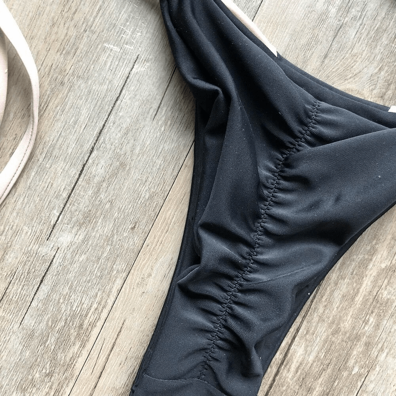 Stylish black low-waisted lace-up swimsuit on wooden background, perfect for beach days and pool parties.