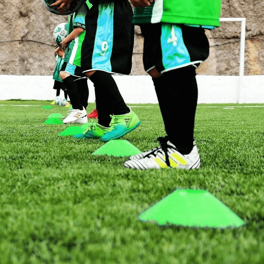 Athletes training with green cones on a soccer field using speed and agility equipment for improved performance.
