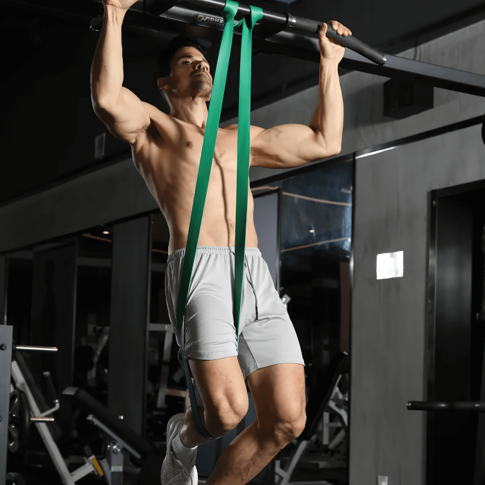 Man using green resistance band for pull-ups in a gym setting, showcasing strength training and flexibility enhancement.