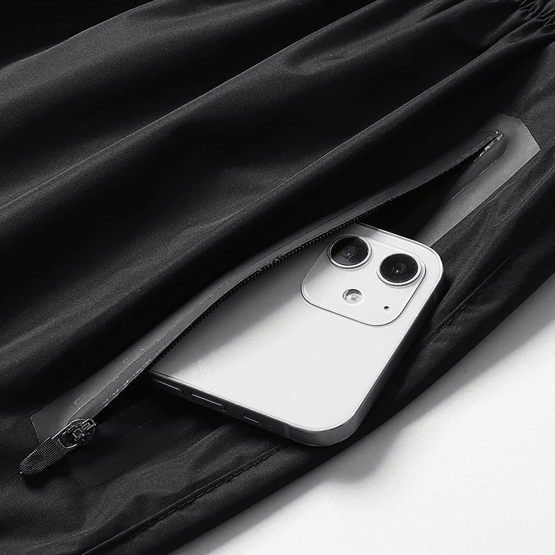 Close-up of a men's black running tracksuit pocket with a secure zippered closure holding a smartphone inside.