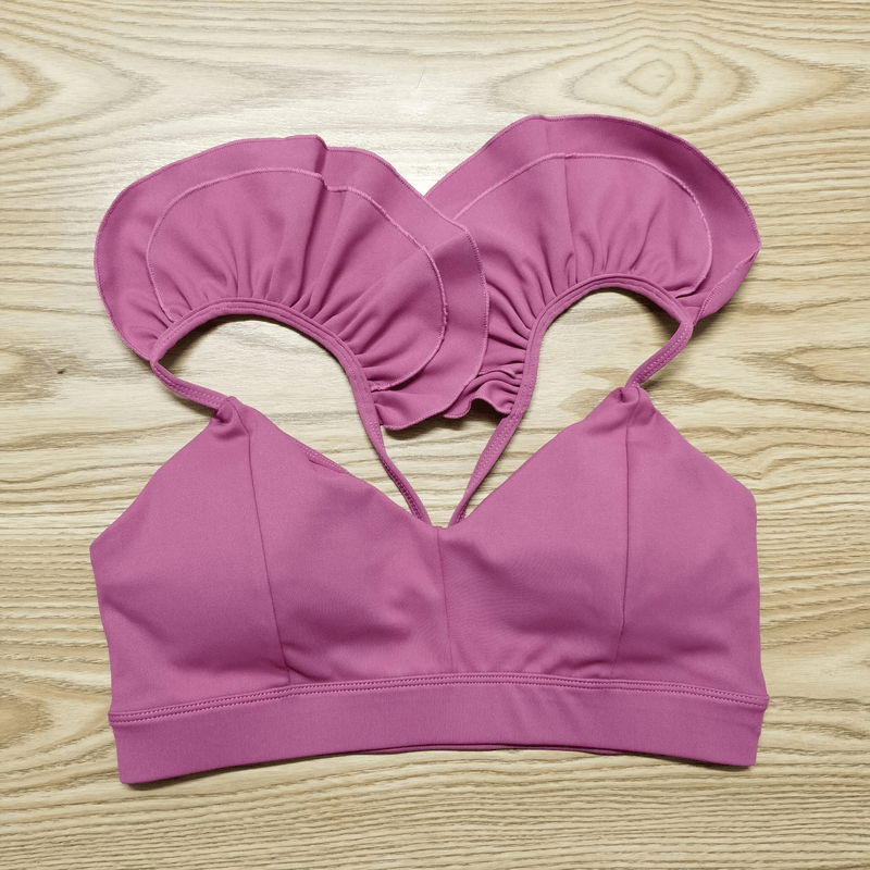 Pink quick-dry sports bra with ruffled straps on wood background, designed for female athletes' comfort and performance.