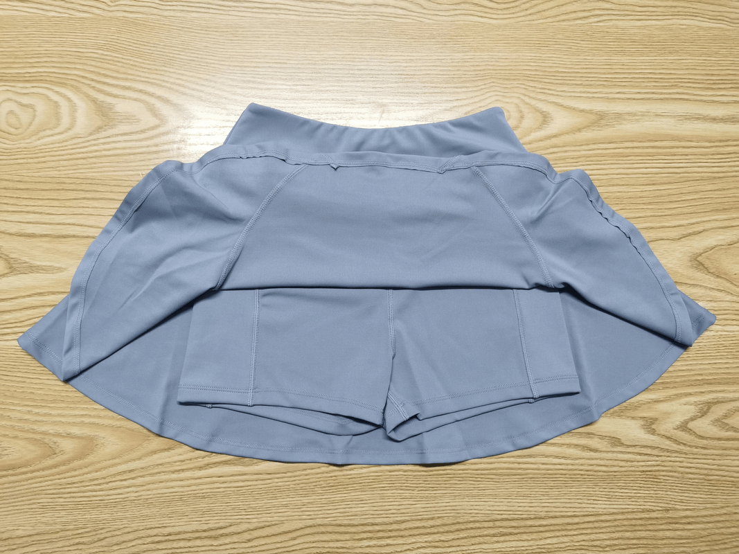 Blue quick dry skirt-shorts with solid pattern for female athletes on a wooden background, ideal for running and tennis.