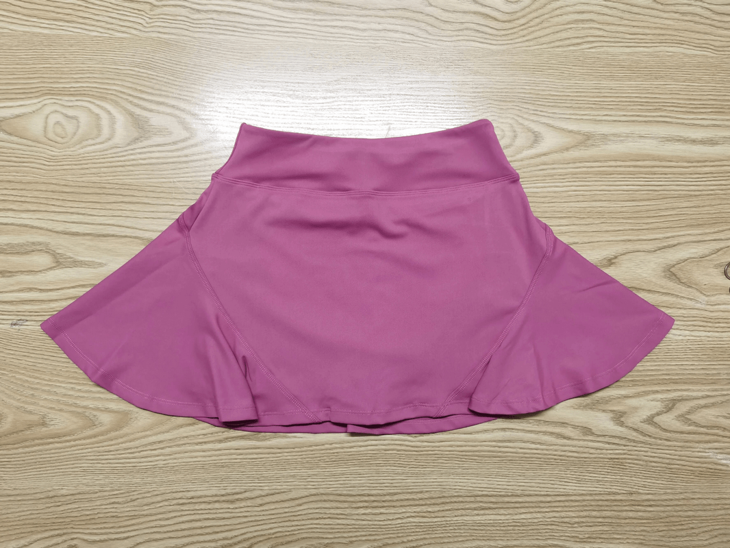 Pink skirt-shorts with quick-dry, breathable nylon fabric on wooden background, ideal for sports and activewear.