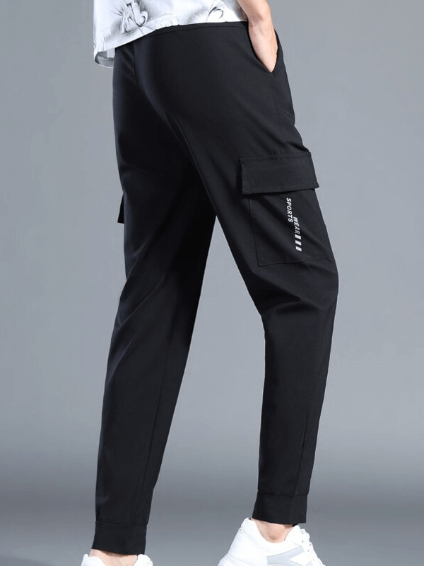 Man wearing quick-drying black sports pants with side pockets, ideal for running, showcasing full-length design and elastic waistband.